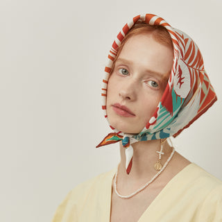 Silk bandana with vibrant coral and teal botanical zebra print worn as a head scarf, displaying luxury hand-rolled edges against soft yellow attire