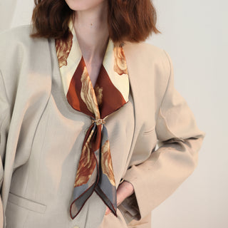 Woman wearing Berlin Rose silk scarf – 65cm vintage floral square bandana in sepia tones, styled over a beige blazer.
