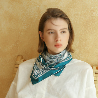 Teal Heritage Grace silk scarf with intricate blue and white pattern worn as neck accessory with white linen outfit against warm beige background