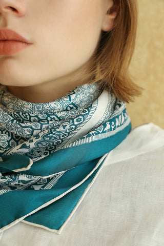 Teal Heritage Grace silk scarf wrapped elegantly around neck, showcasing intricate bird and floral pattern with hand-rolled white border on luxurious twill fabric