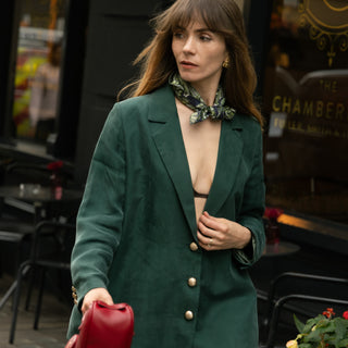 Woman wearing a navy and green patterned silk scarf in a green blazer holding a red handbag on a street.