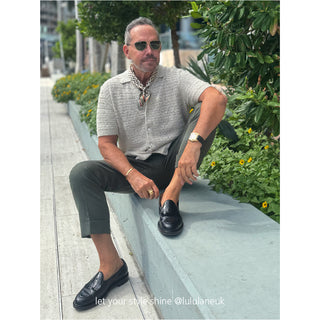 Luxury silk scarf styled as neckerchief with geometric pattern, worn with light knit polo in urban garden setting