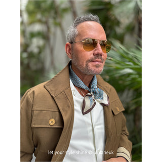 Stylish light blue silk bandana with geometric pattern worn as neckerchief with tan jacket and white shirt, showcasing versatile accessory styling