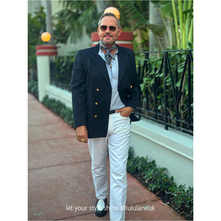 Navy silk paisley scarf worn as a stylish neckerchief with navy blazer and white pants in tropical setting, showcasing versatile smart causal styling