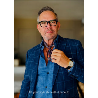 Blue checkered blazer with colorful plum and orange geometric silk neckerchief styled with denim shirt and gold watch, showcasing elegant men's fashion