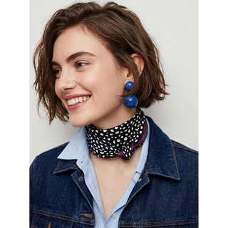 Woman wearing a spotted pattern silk scarf in black and white styled as a versatile neck scarf