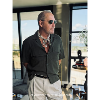 Man wearing white burgundy geometric silk bandana with green shirt and white pants in modern interior with panoramic windows
