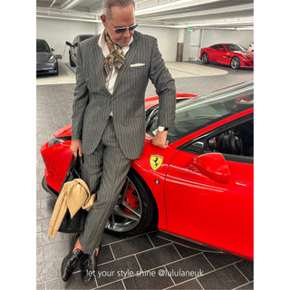 Man wearing Amazon Toucan organic cotton-silk scarf in a pinstripe suit — classic, refined style, standing next to a red Ferrari in a garage 