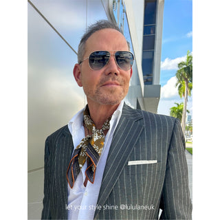 Man wearing Amazon Toucan organic cotton-silk scarf in a pinstripe suit with sunglasses — classic, refined style, standing outdoors.