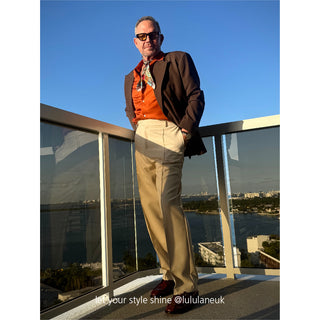 Bohemian silk scarf styled as neckerchief with brown blazer, orange shirt and beige pants on balcony with city view