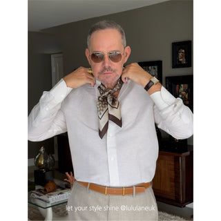Men’s heritage geometric silk scarf in brown and beige tones styled with a linen shirt and pleated trousers; refined, classic look with warm neutrals.