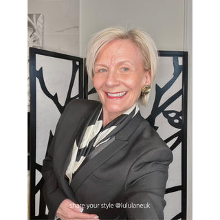 Elegant black and white silk camellia scarf styled with dark blazer, showcasing luxurious twill fabric against decorative black and white background