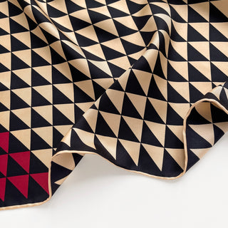 Close-up of a beige and black geometric triangle silk bandana with red corner, 53cm square with hand-rolled hems.