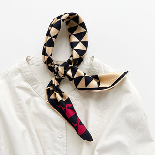 Beige and black geometric triangle silk bandana with red corner over a cream turtle neck shirt.