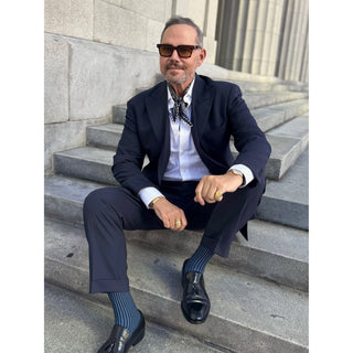 Man wearing a navy paisley patterned silk square neckerchief by LuluLane with a navy suit and sunglasses showcasing a refined sharp look.