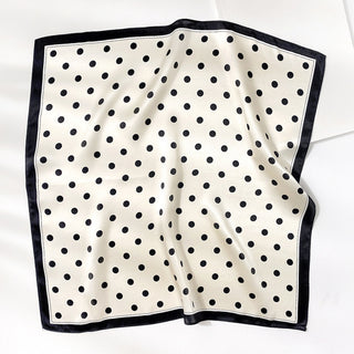 Square silk bandana scarf with cream background and classic black polka dots, finished with navy blue border trim, displayed flat