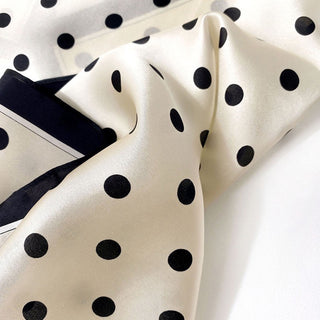 Luxurious white silk scarf with black polka dots and navy blue border, showcasing shiny fabric texture and elegant pattern detail