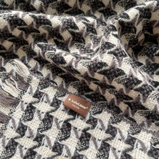 Close-up of a taupe, black and cream white cashmere scarf with houndstooth check pattern and LuluLane label
