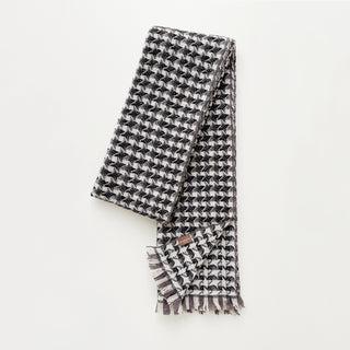 Folded cashmere scarf in taupe, black and cream white with houndstooth check pattern on a light grey background