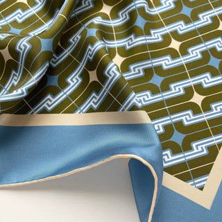 Close-up of a men's luxury silk square scarf featuring retro geometric pattern in dusty blue, olive green and cream white with hand-rolled edges.