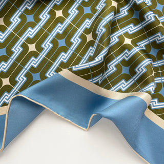 Close-up of a men's luxury silk square scarf featuring retro geometric pattern in dusty blue, olive green and cream white with hand-rolled edges.