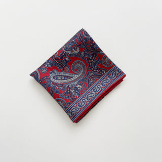 Folded men’s silk neckerchief scarf in red and navy paisley pattern, double-sided with hand-rolled edges.
