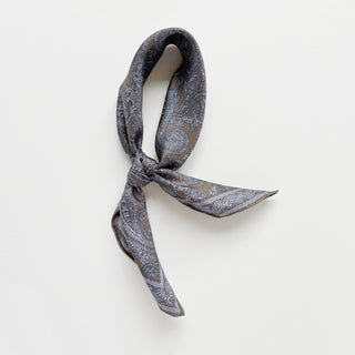 Men's silk neckerchief in taupe featuring paisley pattern tied into a knot on a light grey background
