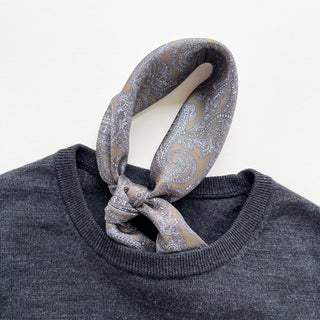 Men's silk neckerchief in taupe featuring paisley pattern tucked in a dark grey sweater.