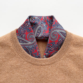 Beige sweater with a red and navy paisley patterned silk neckerchief scarf around the neck on a light grey background