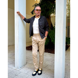 Man wearing unisex chess board pattern silk square scarf in golden squash yellow and navy by LuluLane in dark blue racer jacket, beige trousers and a pair of leather loafers.