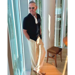 Man wearing an ivory paisley pattern silk bandana square by LuluLane in dark blazer and white trousers with sunglasses showcasing a refined, smart causal look.