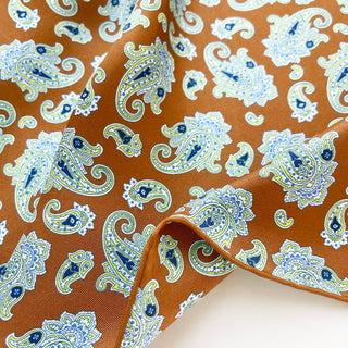 Close-up of a honey brown paisley men’s silk neckerchief scarf – luxurious silk twill fabric with blue, white and yellow paisley pattern