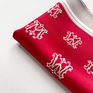 Vibrant red silk square scarf with elegant white crown pattern throughout and white border trim, displayed folded on white surface.