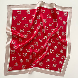 Red silk square scarf with repeating crown monogram pattern and elegant beige border, displayed with gentle folds showing its luxurious texture