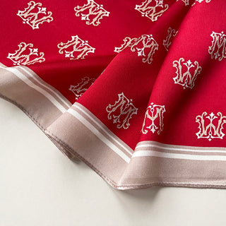 Red silk scarf with repeating white crown pattern and beige border trim, elegantly folded showing luxurious texture and detail