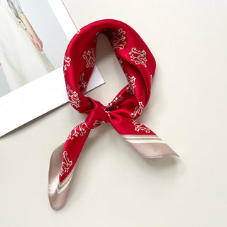 Vibrant red silk square scarf with white crown pattern, tied in neckerchief style, featuring beige border accents against neutral background