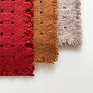 Three pure cashmere scarves featuring openwork jacquard design in red, mustard brown, and beige on a light grey background.