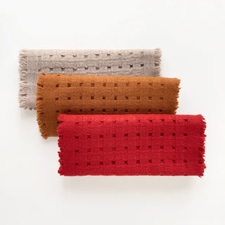 Three pure cashmere scarves featuring openwork jacquard design in red, mustard brown, and beige on a light grey background.