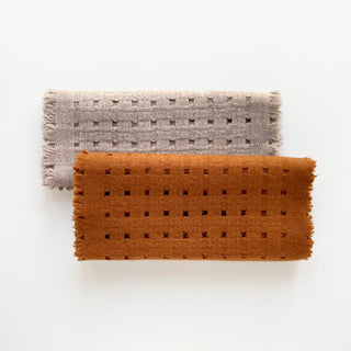 Two pure cashmere scarves featuring openwork jacquard design in mustard brown and beige on a light grey background.