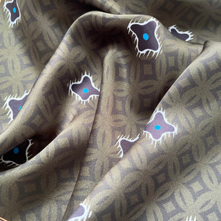 Olive green silk neckerchief with geometric pattern featuring purple star motifs with bright blue centers, displayed in elegant folds showing fabric texture.