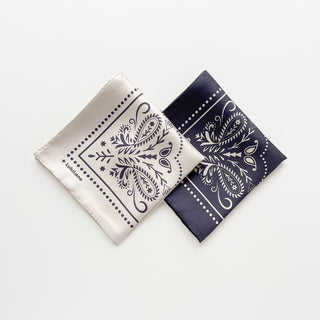 Folded two silk square scarves with double-sided bandana print, one is in ivory, the other is in charcoal grey by LuluLane.