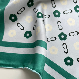 Silk scarf with teal green border and light grey center featuring decorative floral pattern and chain links on luxurious fabric texture