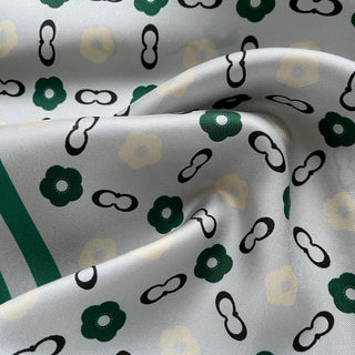 Elegant silk scarf with light grey background featuring teal green flowers and black chain-link patterns, showing silky fabric texture and folds