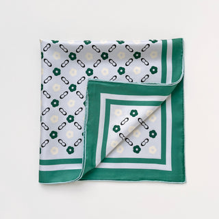 Square silk scarf with light grey background, teal green border, and pattern of green and cream floral shapes with black chain links, folded to display corners