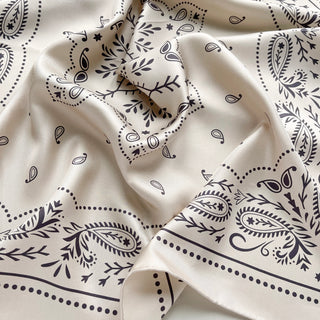 Close-up an ivory silk bandana scarf, 65cm square with modern paisley design and hand-rolled hems by LuluLane.