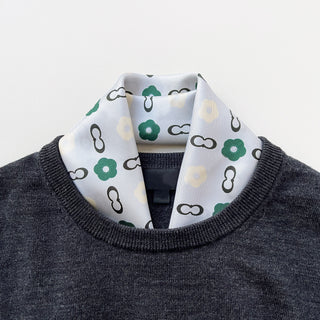 Teal green silk scarf with floral and chain link pattern on light grey background, styled with dark grey sweater showing elegant unisex styling