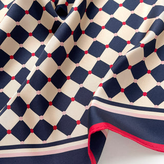 Close-up of a unisex silk scarf 65cm chess board design in navy and ivory with red accents, double-sided silk, hand-rolled edges by LuluLane.