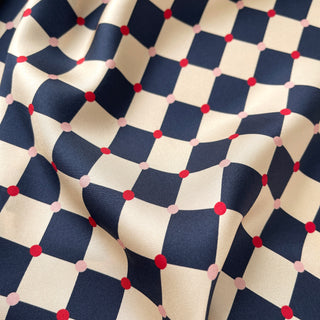 Close-up of a unisex silk scarf 65cm chess board design in navy and ivory with red accents, double-sided silk, hand-rolled edges by LuluLane.