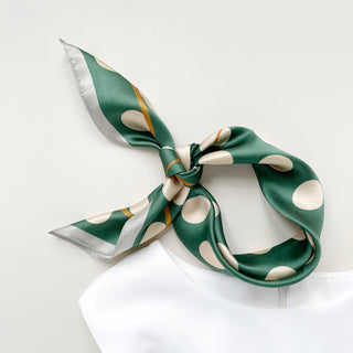 Jade green silk bandana with beige polka dots and gold accents, tied stylishly as a neckerchief against white background
