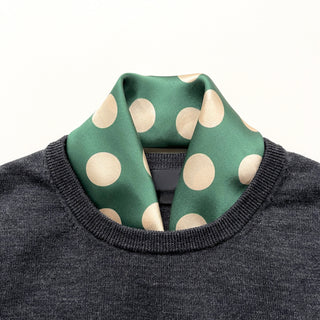 Jade green silk scarf with beige polka dots styled as a neckerchief, worn with dark gray sweater showing elegant contrast and silky texture.